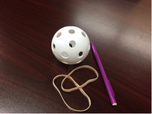 This is a picture of the materials needed: a wiffle ball, mechanical pencil, and elastics