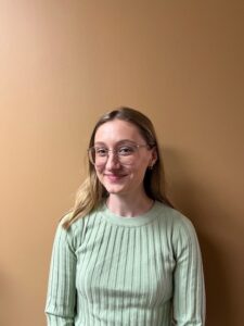 headshot of a young adult with long dark blond hair, light skin, and glasses smiling at the camera